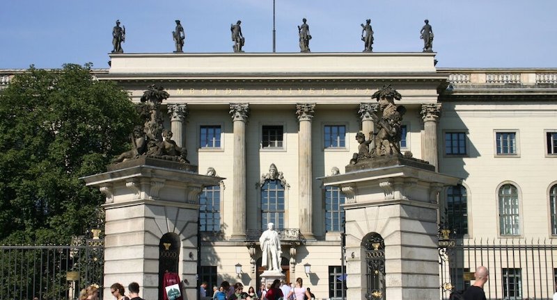 View of main gate of Humboldt University Berlin in Germany. A white Greek style facade with 6 statues on the roof and a sculpture in the middle