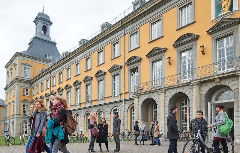 Outside view of University of Bonn in Germany. Yellow colour building with many students standing outside.