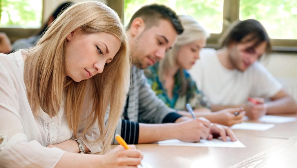 GRE Vs GMAT. 3 students sitting in the exam hall and writing GRE and GMAT test